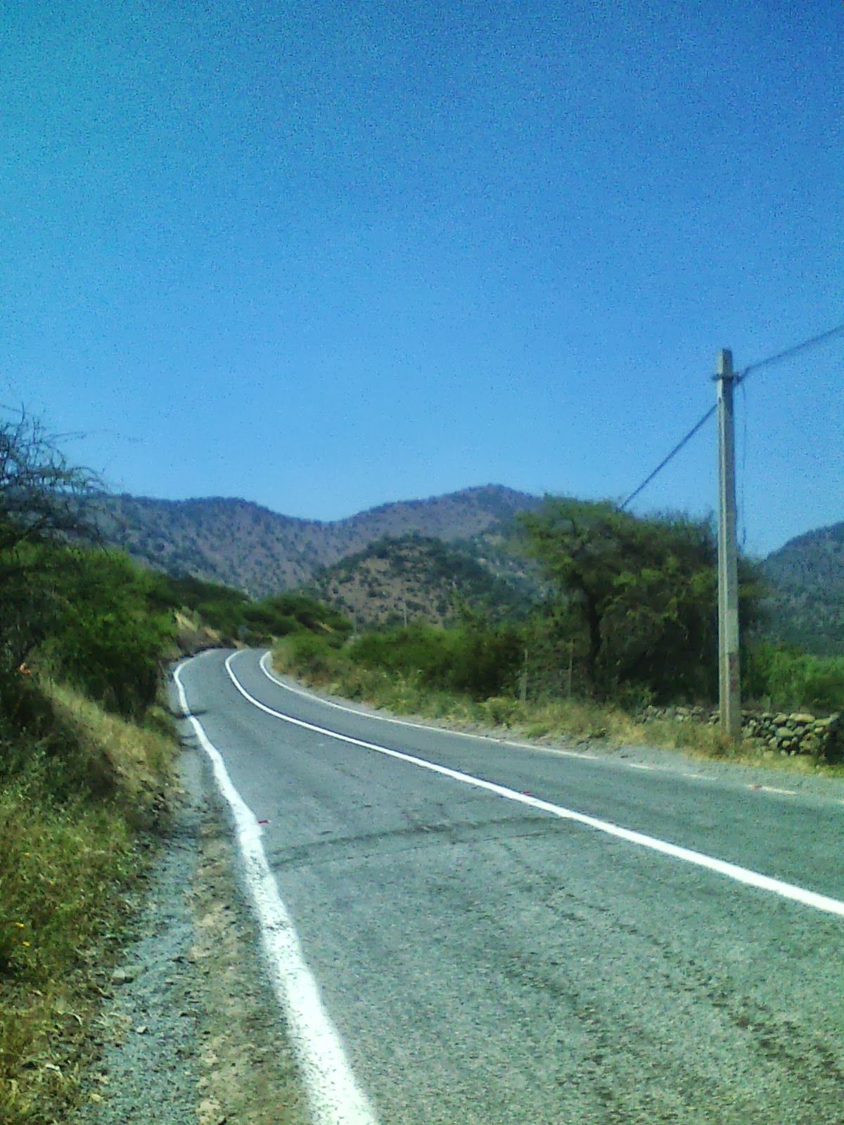 Empty road curving between green hills southeast of Santiago on the way into the Andes foothills