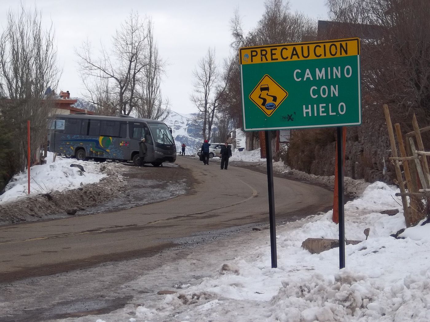 Snowy road to El Colorado and La Parva with a minibus and a yellow Chilean road sign warning of ice