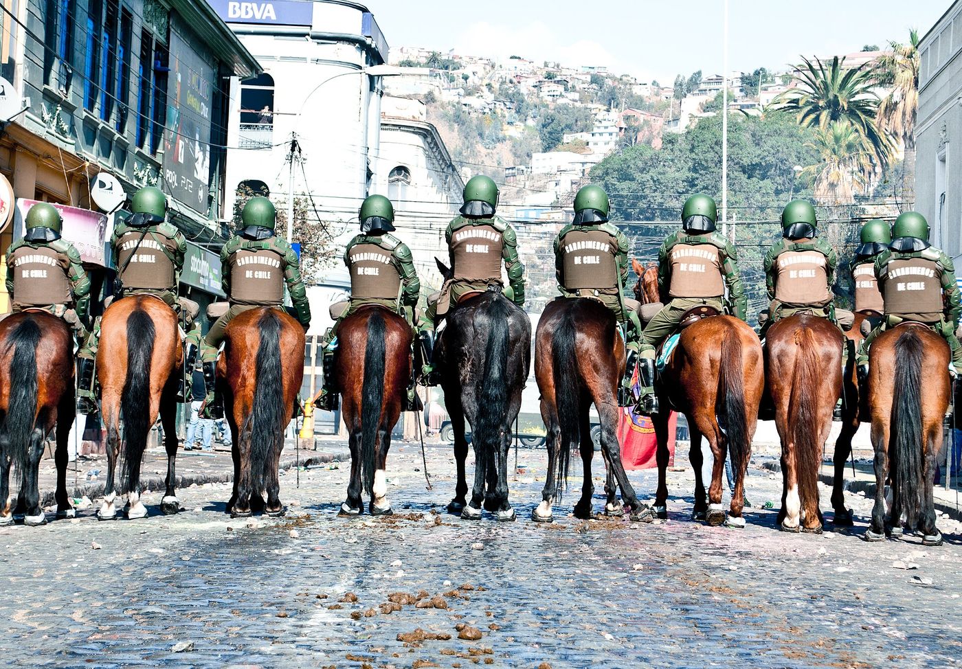 A line of mounted Carabineros in riot equipment forming a cordon across a street in Chile