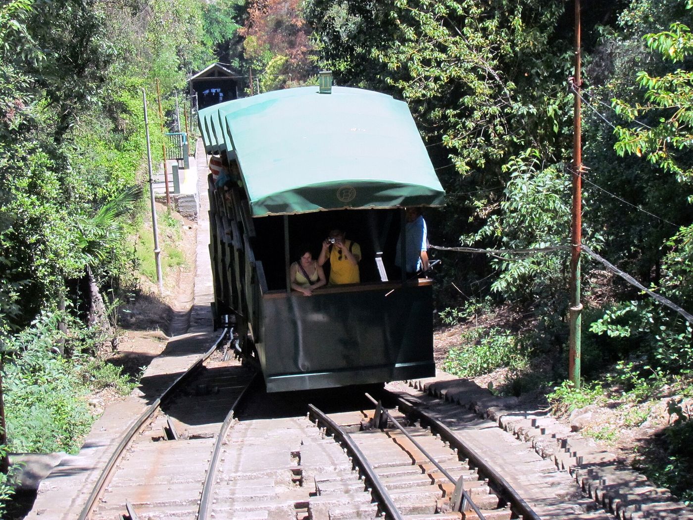 Green wooden funicular car climbing through trees on Cerro San Cristóbal