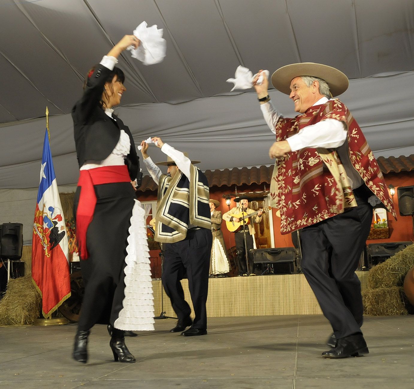 A couple dancing the cueca with white handkerchiefs raised above their heads at a Chilean national celebration
