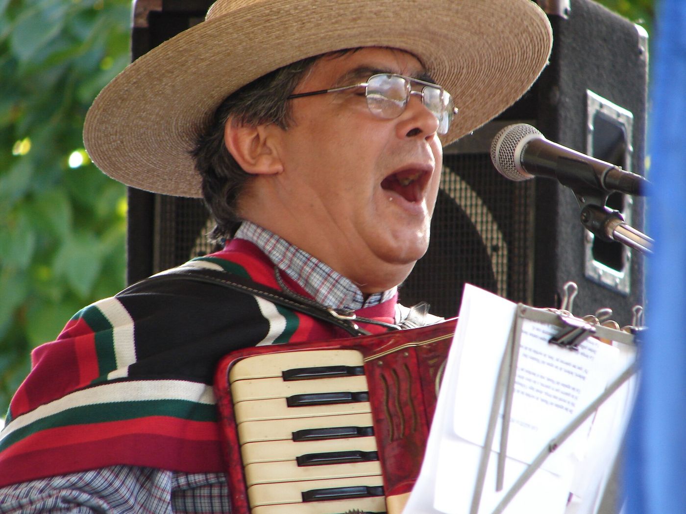 Chilean musician in a straw hat and poncho singing and playing accordion at a Fiestas Patrias celebration