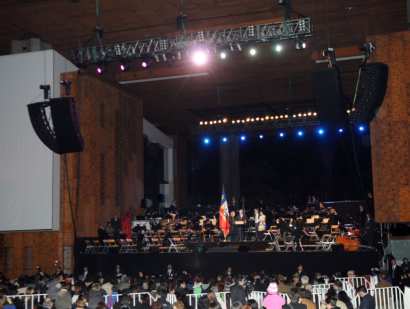 An orchestra performing on a lit stage in front of a seated audience at GAM in Santiago