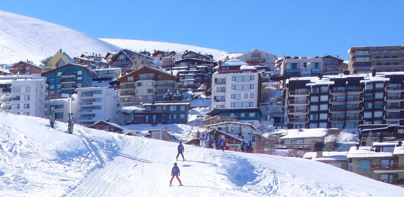 Skier on a piste in front of the chalet village at La Parva ski centre in the Chilean Andes