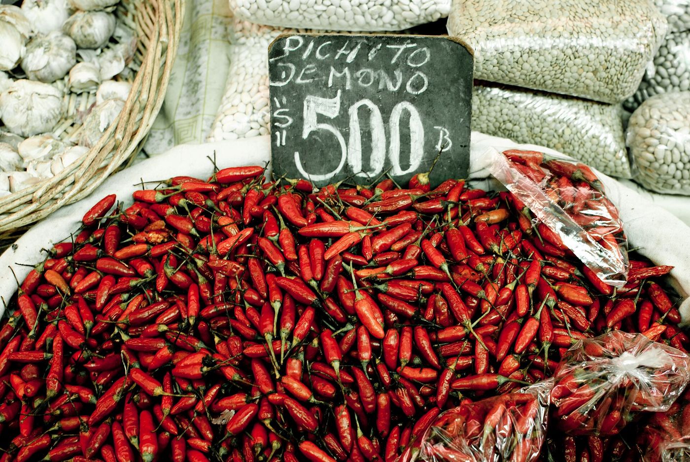 Pile of dried red chillies and sacks of beans and garlic on a stall at La Vega Central, Santiago
