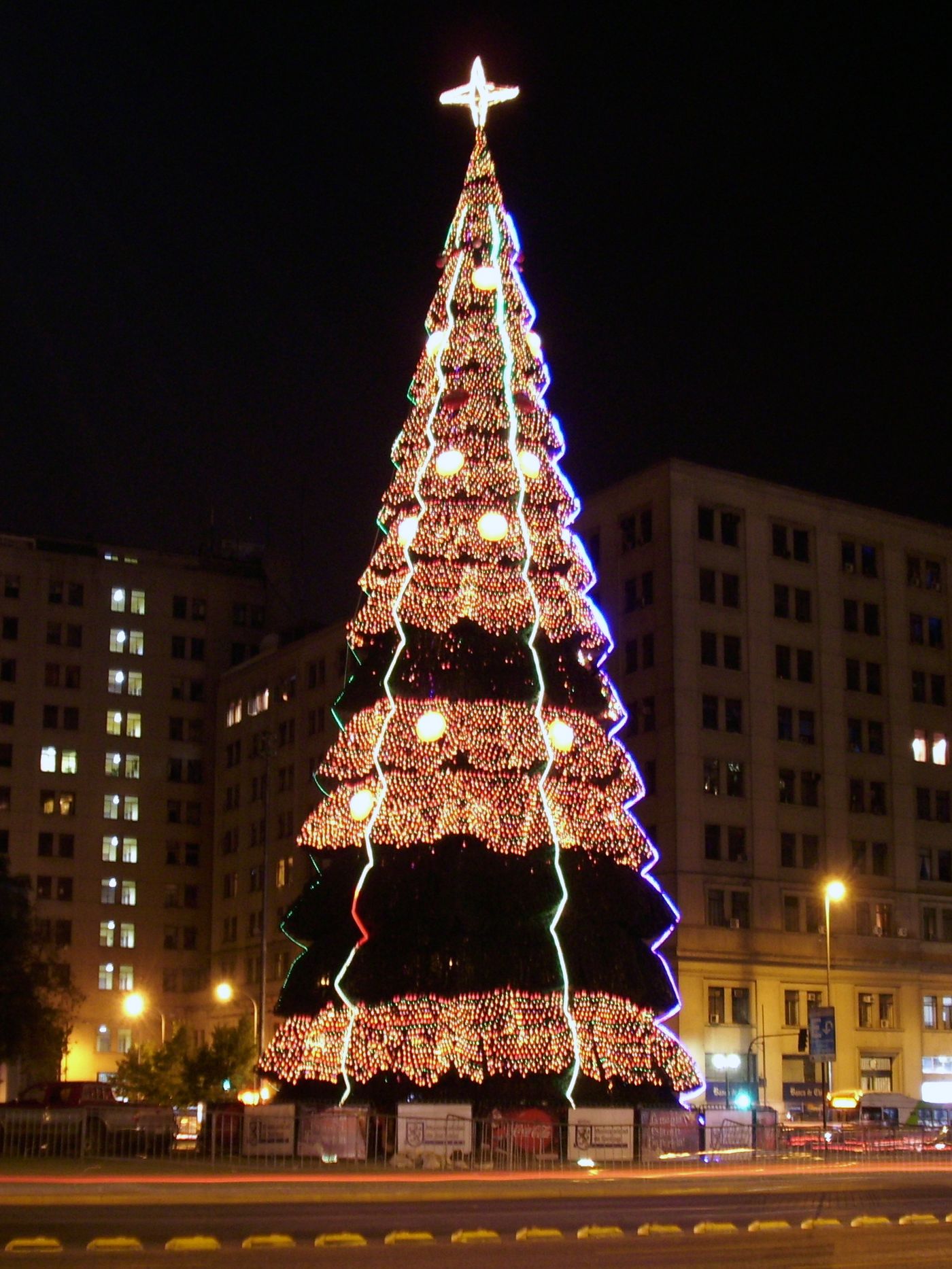 Tall illuminated Christmas tree lit up at night on a Santiago street with buildings behind