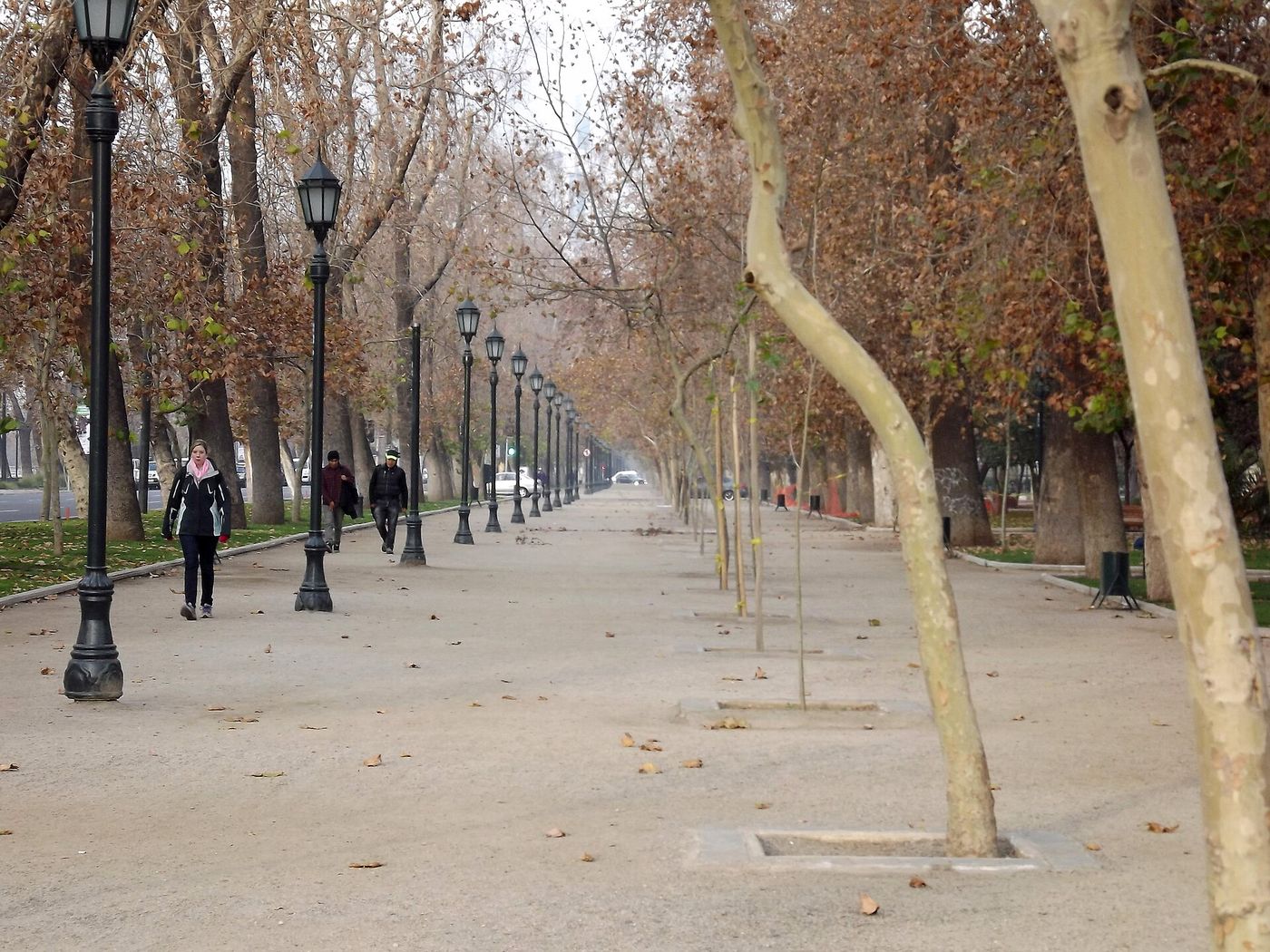 Long flat tree-lined path running through Parque Forestal in central Santiago, with pedestrians in the distance