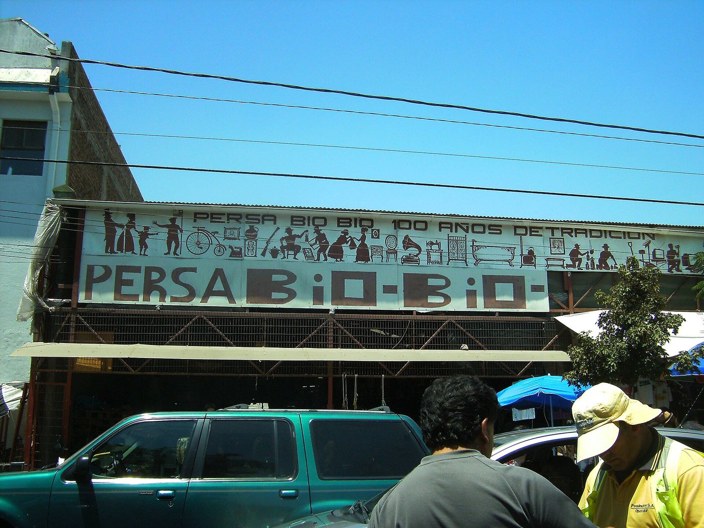 Painted entrance sign reading Persa Bio-Bio above a street of stalls in the Franklin district of Santiago