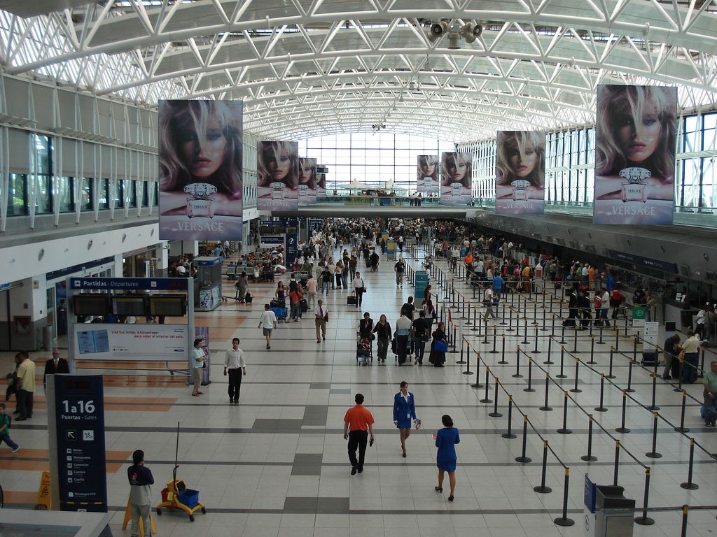 Passengers and queue barriers in the wide check-in hall of Santiago airport under a glass roof