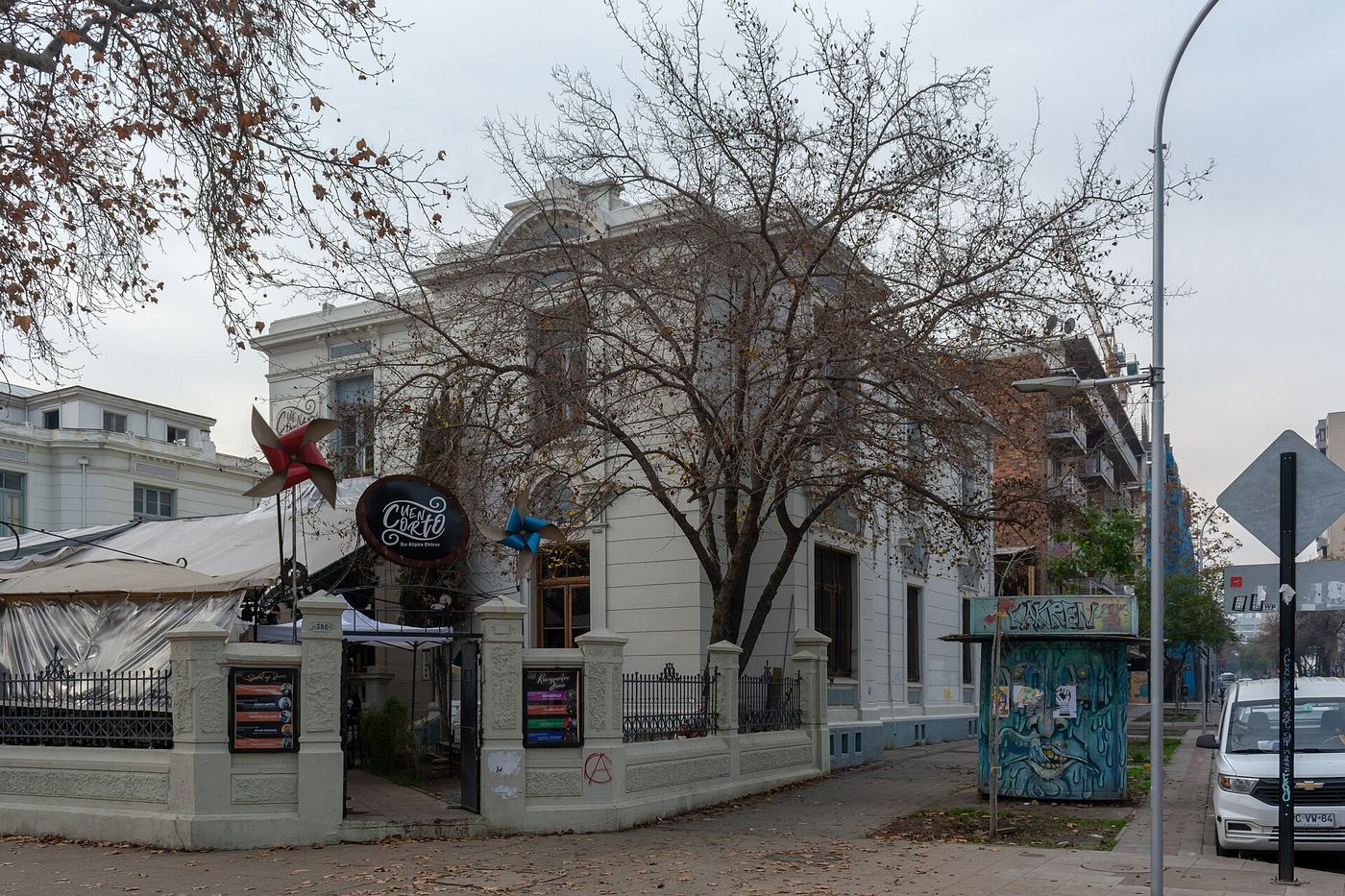 Exterior of a small independent bar in a converted old house in Santiago, with a corner sign and street art on the wall