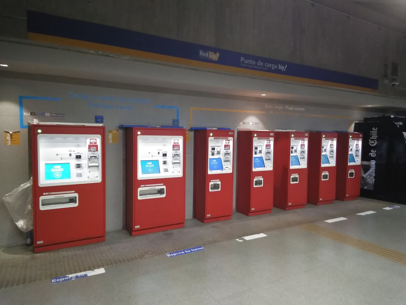 Bank of red self-service bip! card top-up machines inside a Santiago Metro station