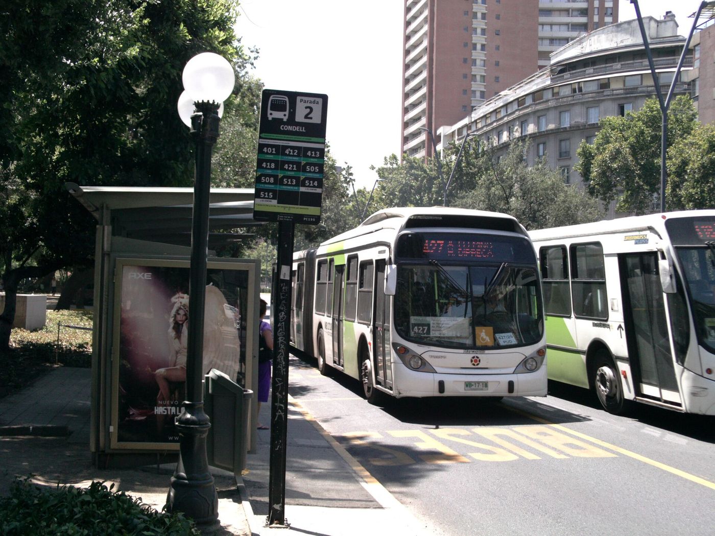 Buses waiting at a covered stop on a Santiago avenue with an electronic arrivals display