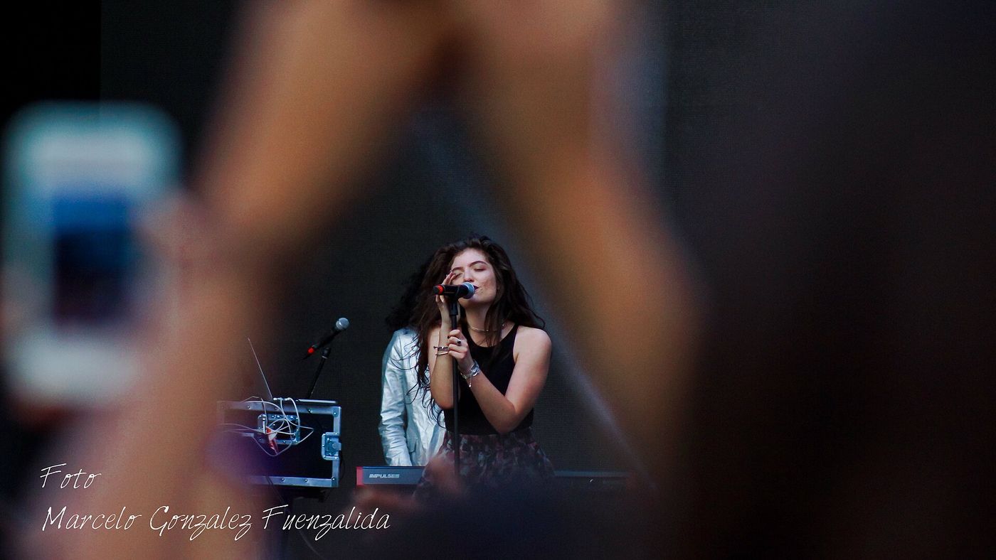 A performer on stage seen through a phone screen held up in the audience at Lollapalooza Chile