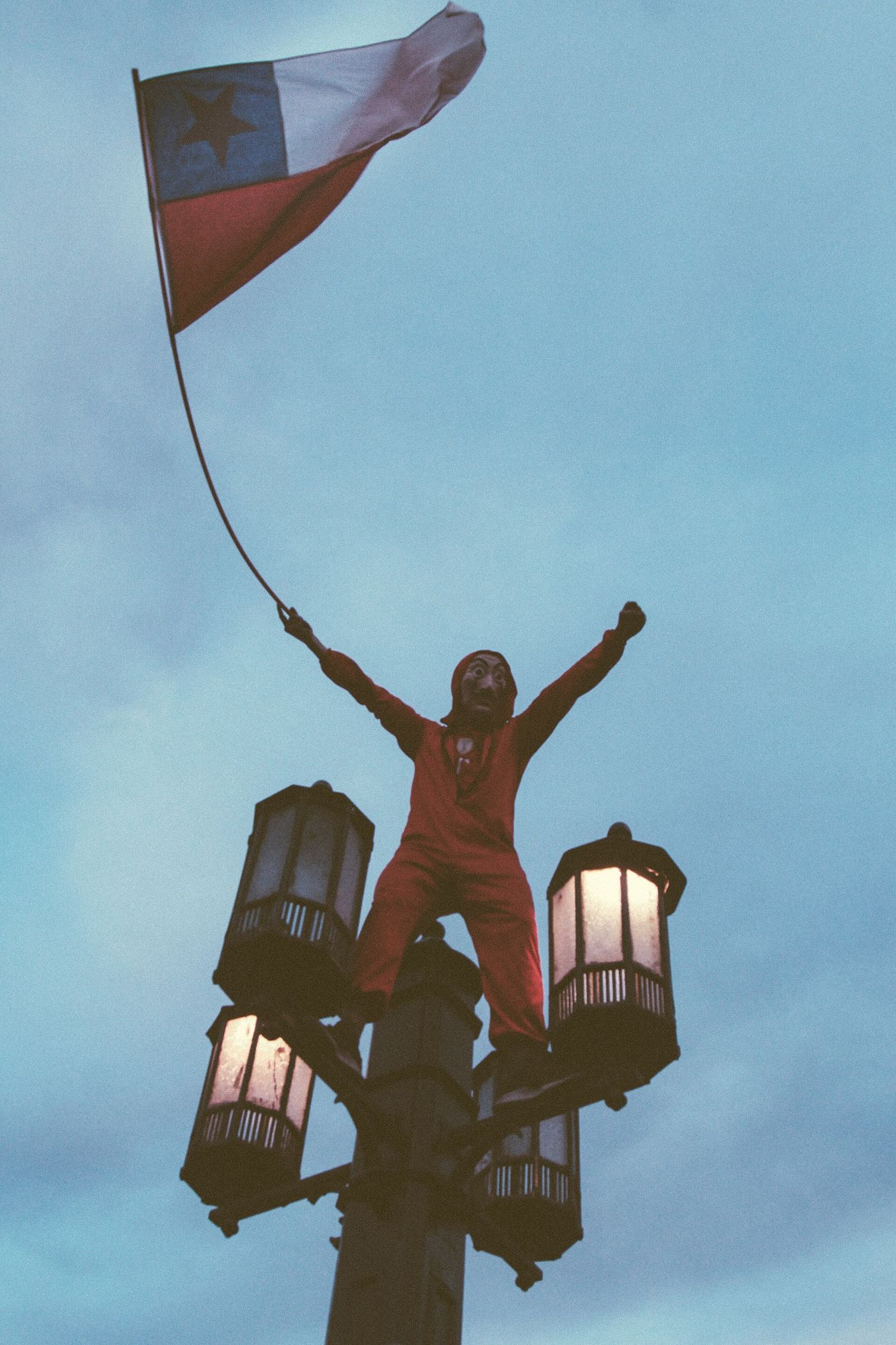 A demonstrator standing on a lamp post waving a Chilean flag above a march