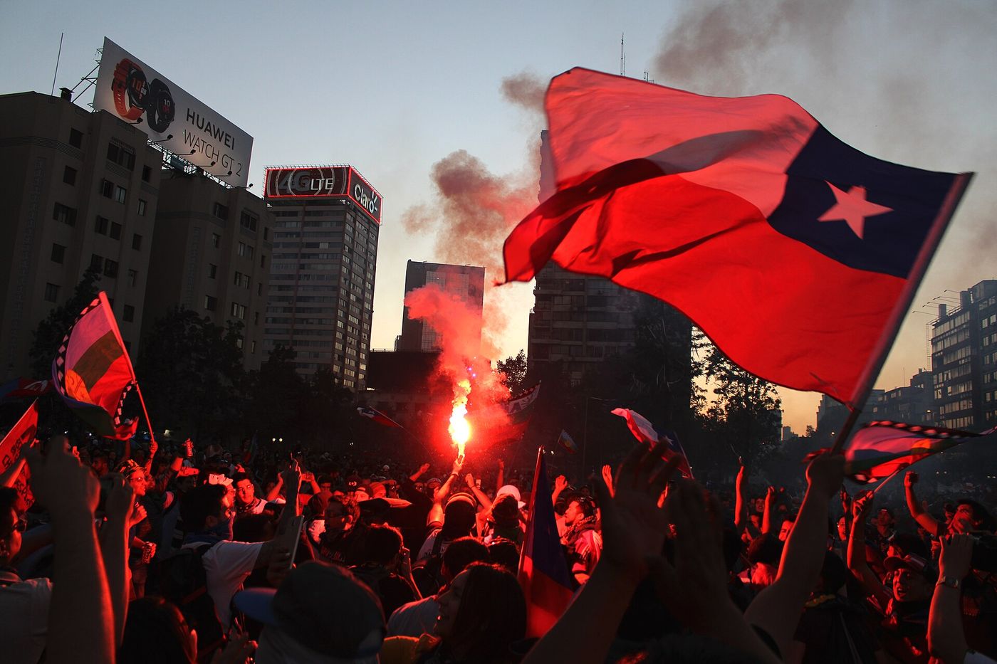Protesters with a Chilean flag and a lit flare at a night demonstration in central Santiago