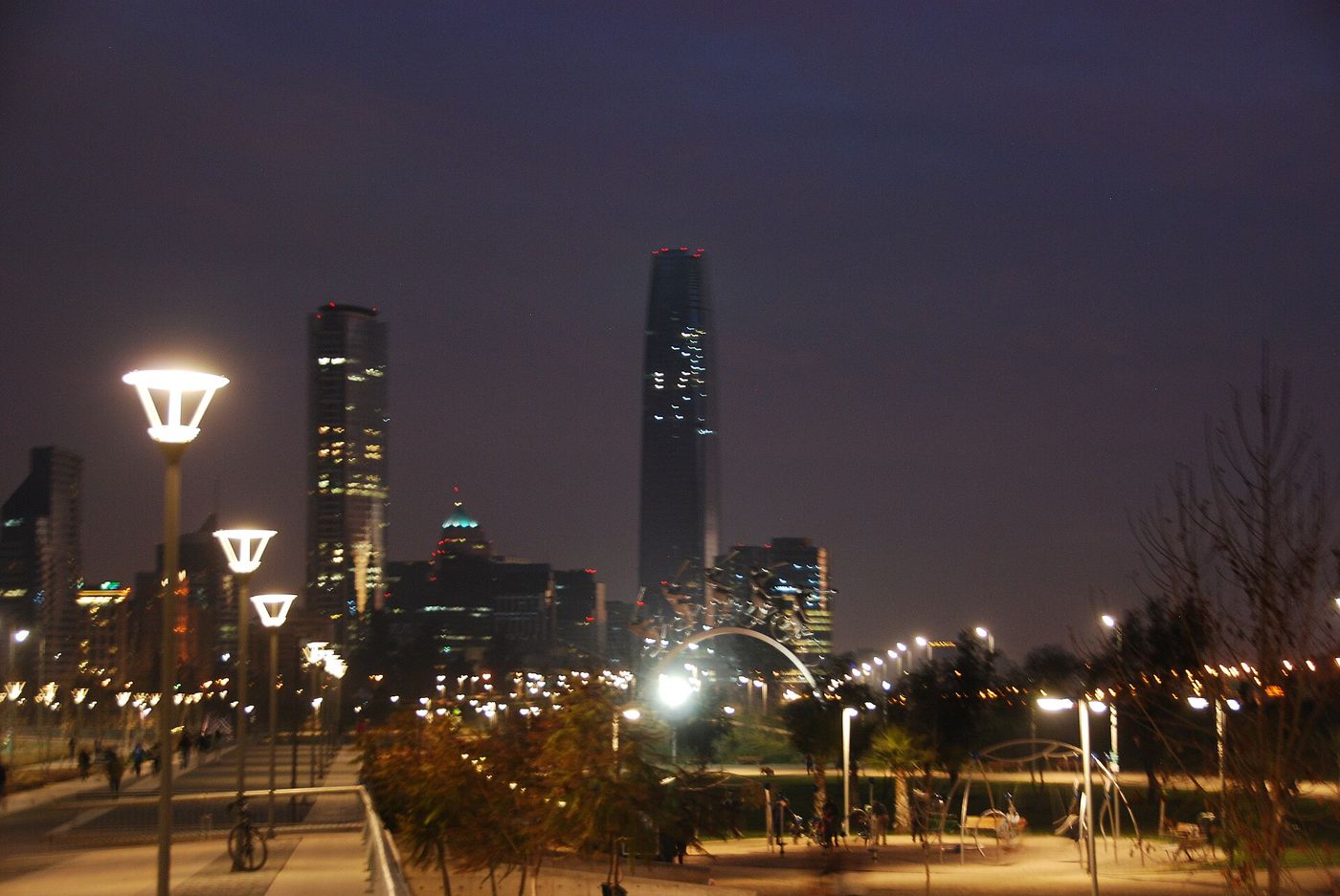 Santiago skyline lit at dusk seen from a park path lined with street lamps