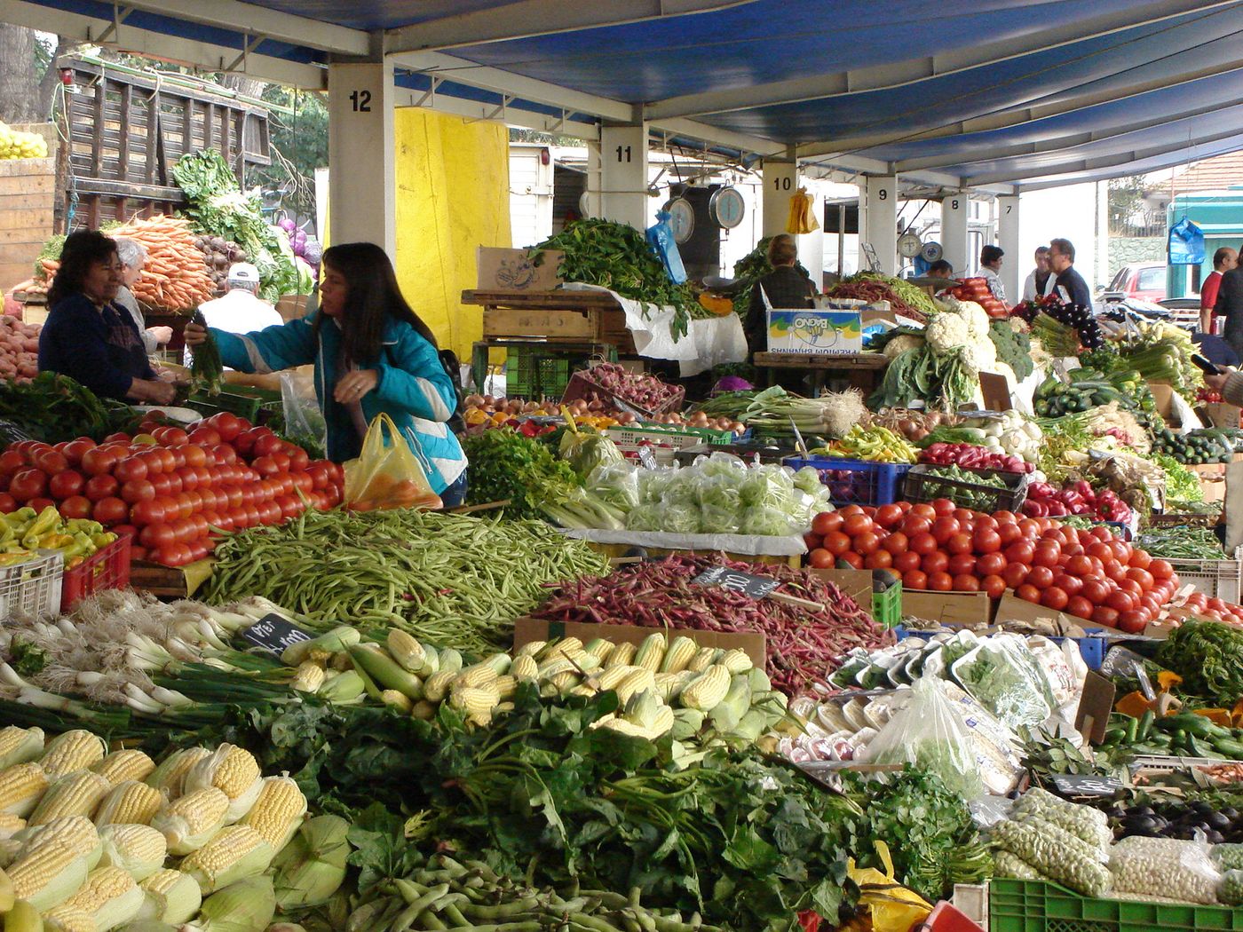 Fruit and vegetable stall piled with produce at a feria libre street market in Santiago, with shoppers browsing