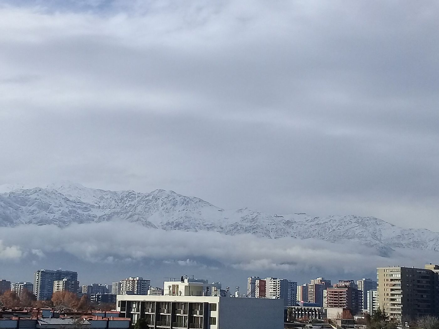 Low grey cloud and fresh snow on the mountains directly above Santiago apartment blocks