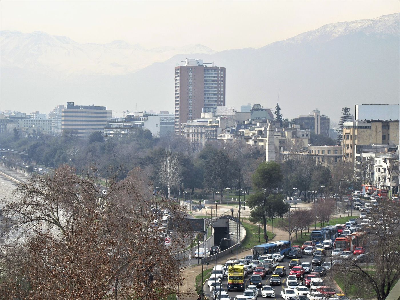 Traffic on Avenida Providencia between apartment towers and trees, with the Andes in haze behind