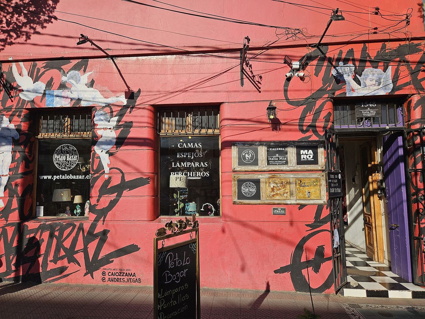 A red shop front painted with black graffiti lettering and murals in Barrio Italia