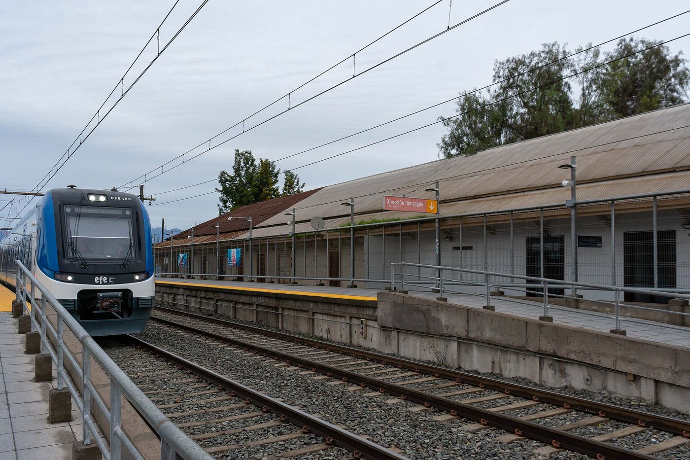 A blue and white commuter train at the platform of Buin station beside the old station building