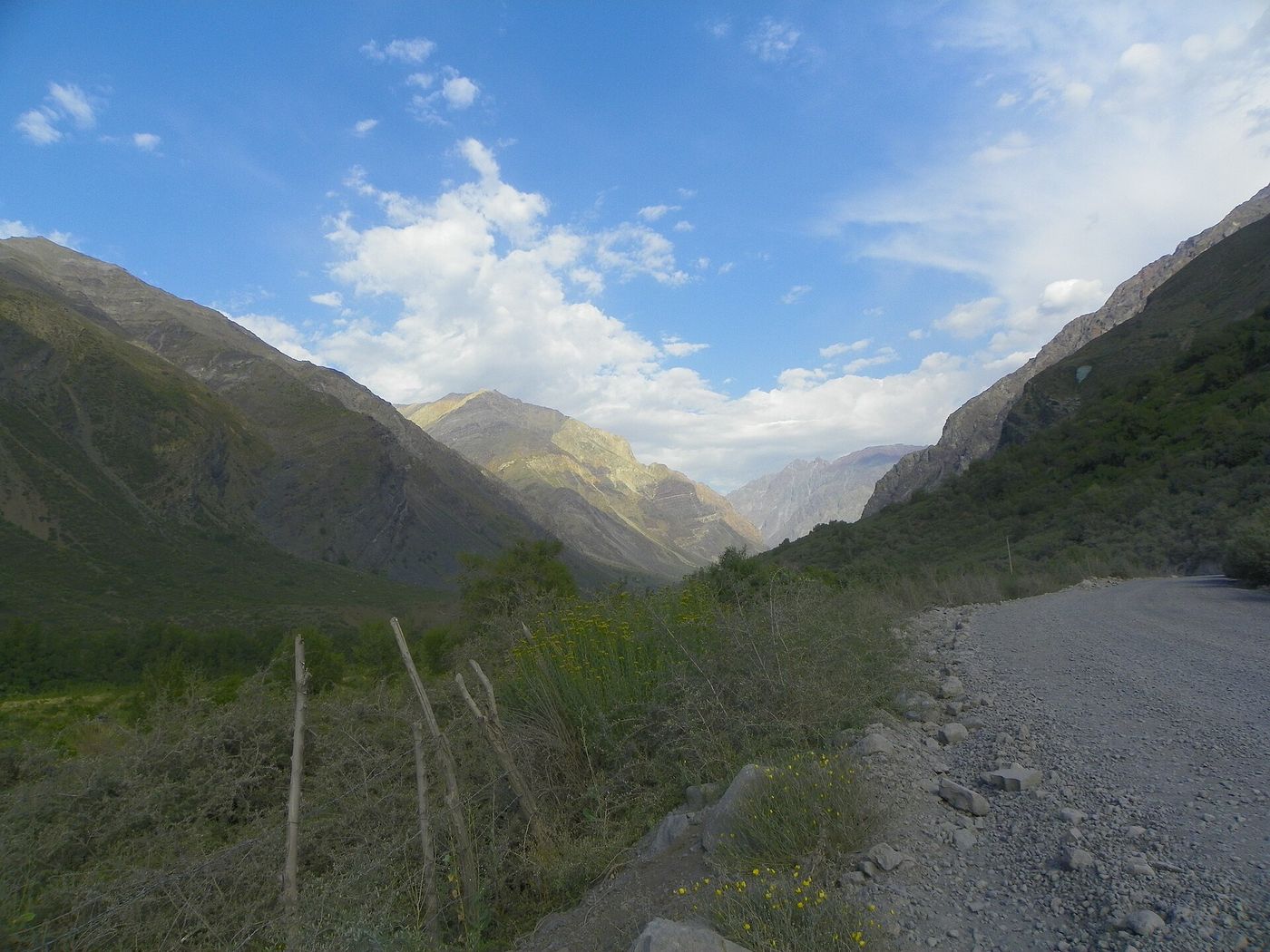 A gravel track running up a green Andean valley in the Cajón del Maipo under scattered clouds