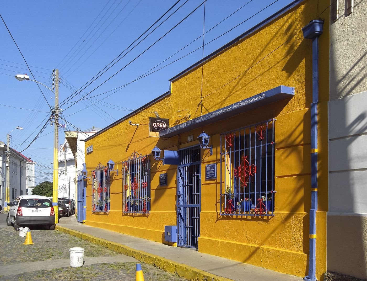 A bright yellow house with blue window frames and iron grilles on a sunny street on Cerro Alegre