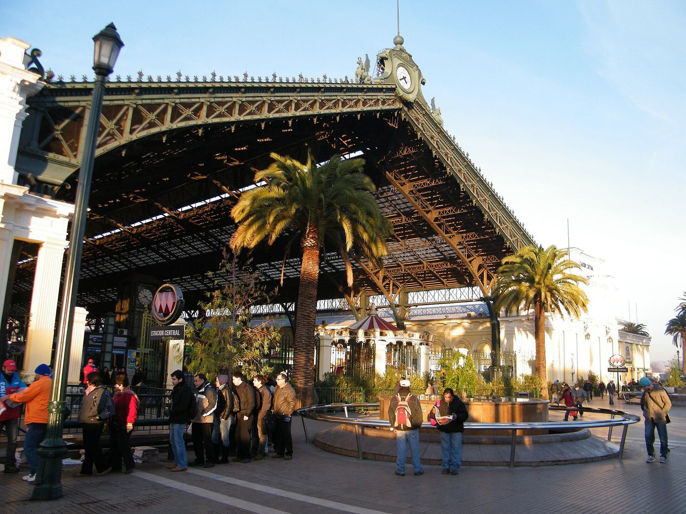 The iron-roofed entrance to Estación Central with palm trees and a Metro sign in the morning