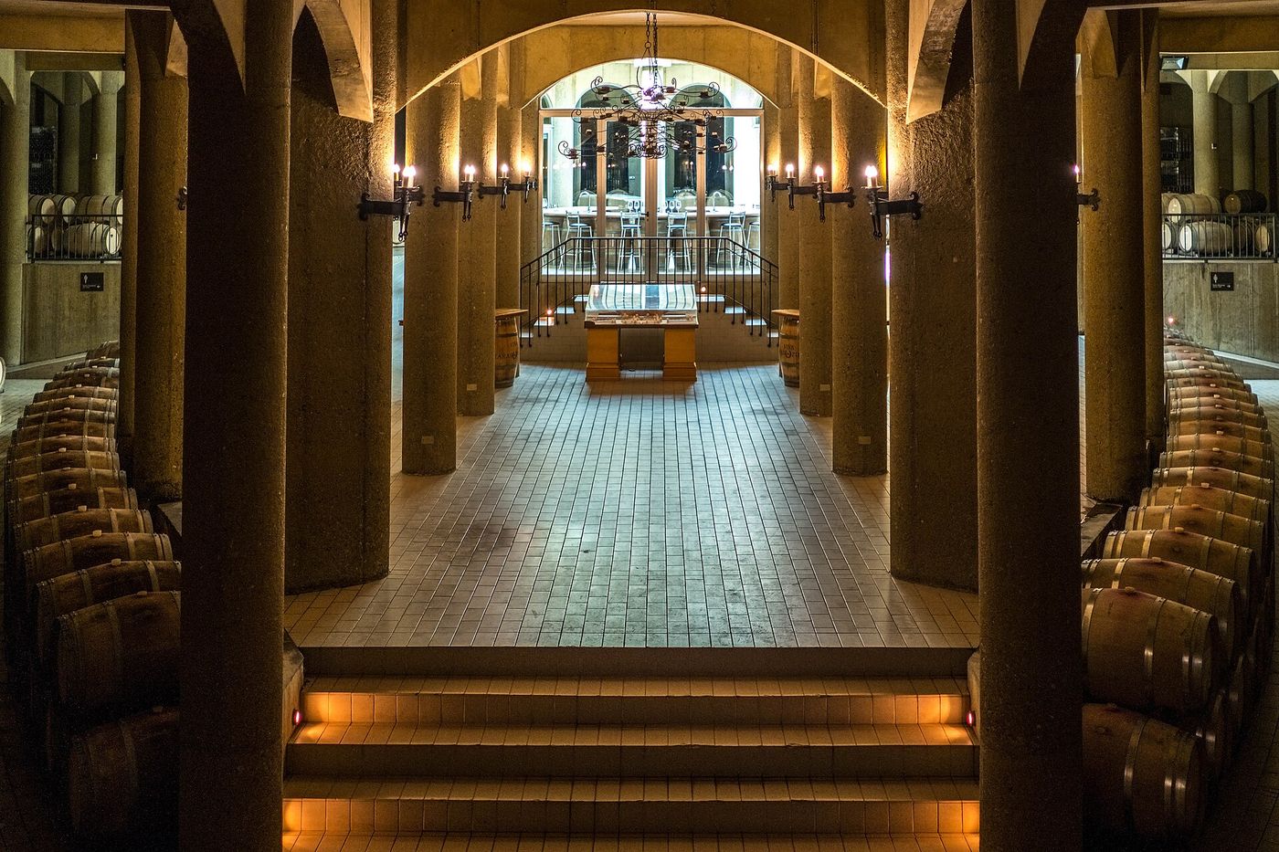 A lit corridor between stacked oak barrels in the cellar at Viña Haras de Pirque
