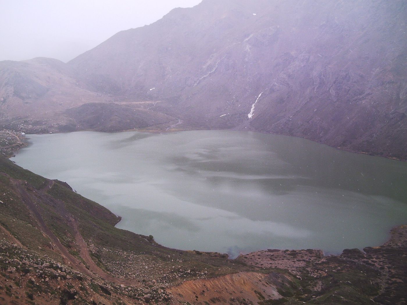 Laguna El Encañado, a gray-green mountain lake below steep slopes in mist