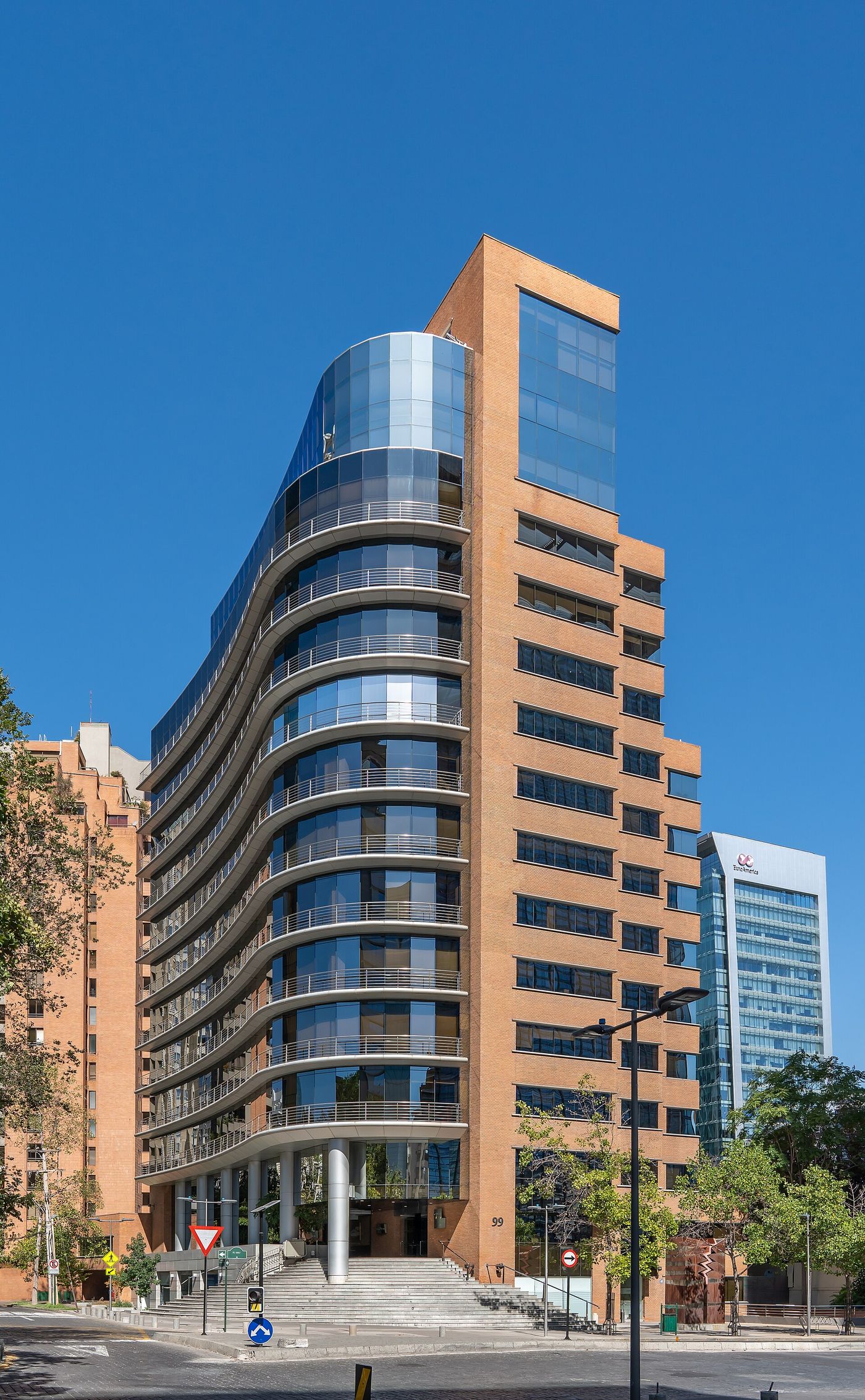 A curved glass and brick office tower on a sunny street in Las Condes