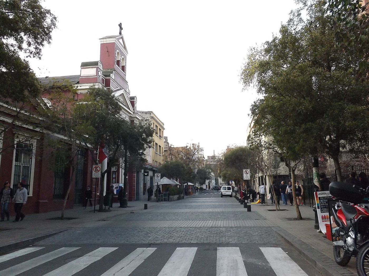 A quiet street in Barrio Lastarria in the morning, with a church tower at the end and parked motorbikes