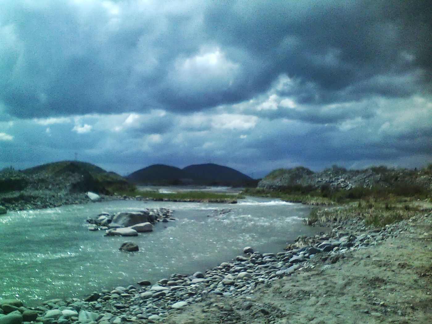 The stony bed of the Maipo River near Buin under heavy clouds, with low hills beyond
