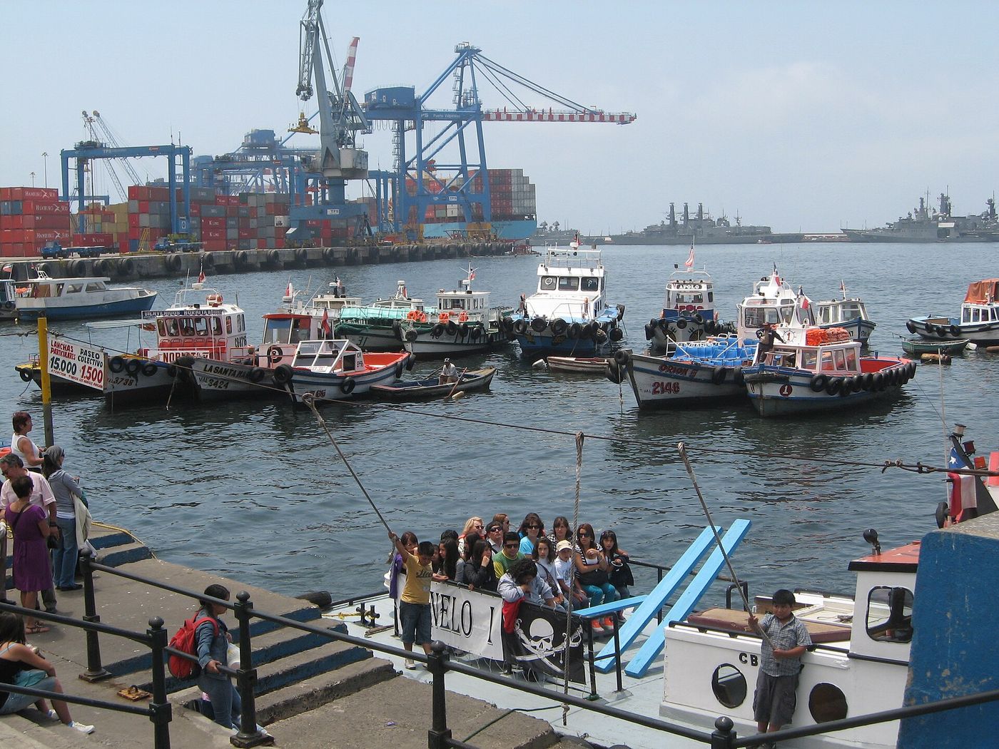 Small boats moored by the Muelle Prat pier with container cranes of the working port behind