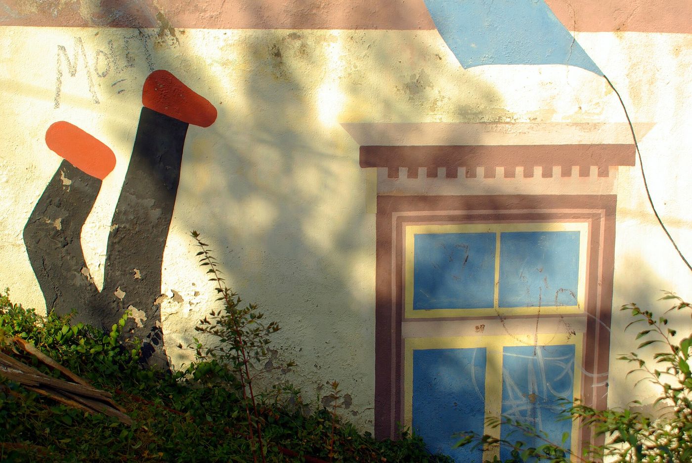 Detail of a painted mural with a window and a figure in red shoes on a house wall in the Museo a Cielo Abierto
