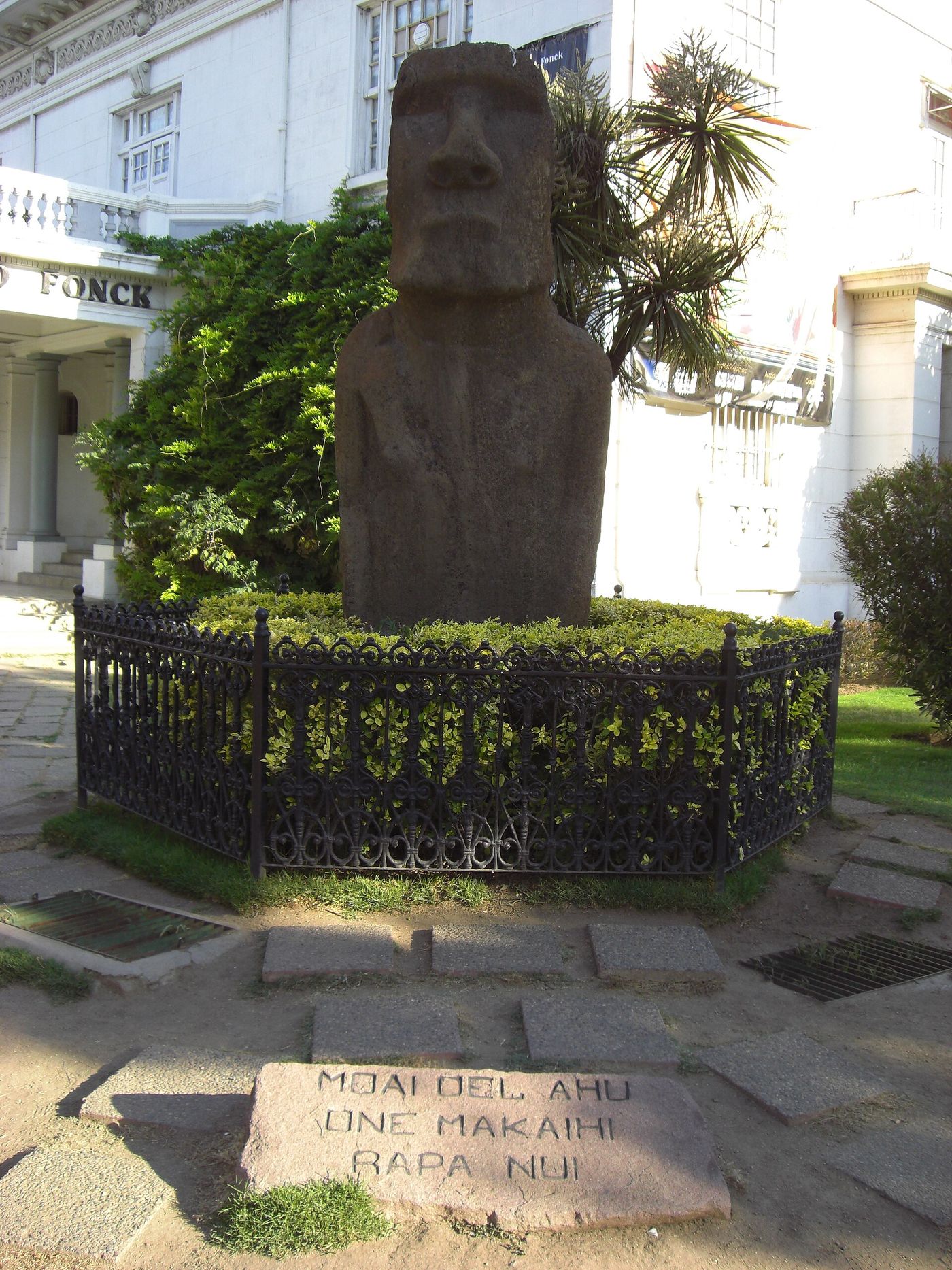 An Easter Island moai standing on a planted plinth behind an iron railing in front of the Museo Fonck