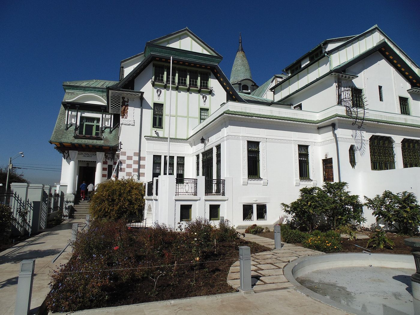 The white Art Nouveau Palacio Baburizza with green turrets and a garden in front on Cerro Alegre