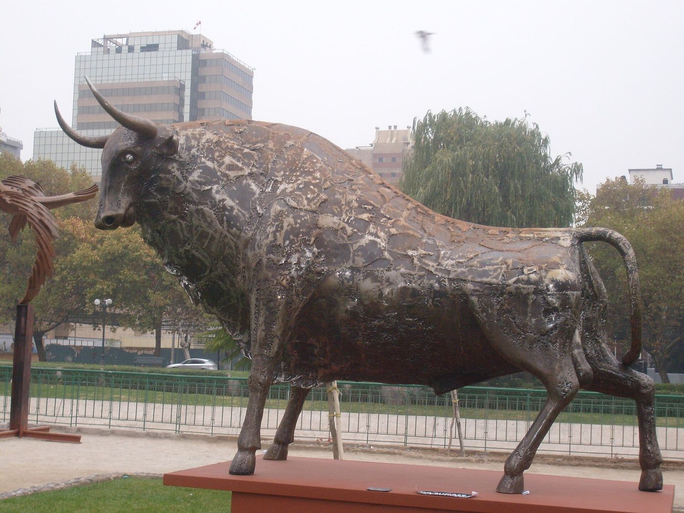 A bronze bull sculpture on a lawn in the Parque de las Esculturas, with office towers behind