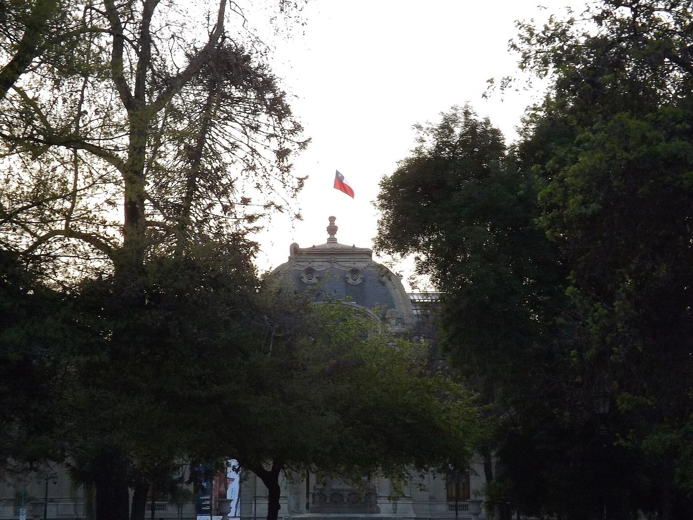 Trees in Parque Forestal framing the dome of the Museo Nacional de Bellas Artes with a Chilean flag on top