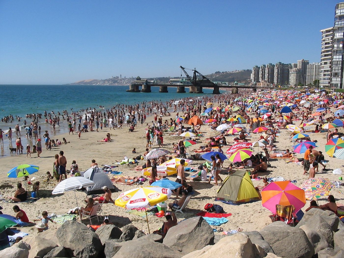 A crowded summer beach in Viña del Mar packed with colorful umbrellas, with apartment towers along the shore