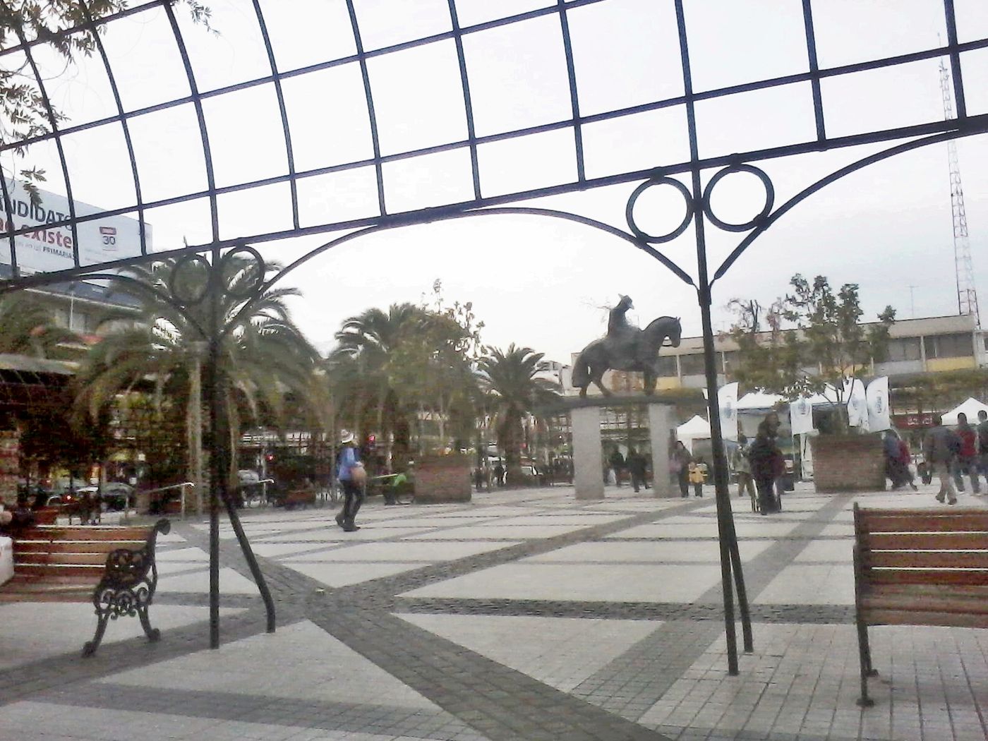 The paved Plaza de Armas of Puente Alto with palm trees, benches and an equestrian statue
