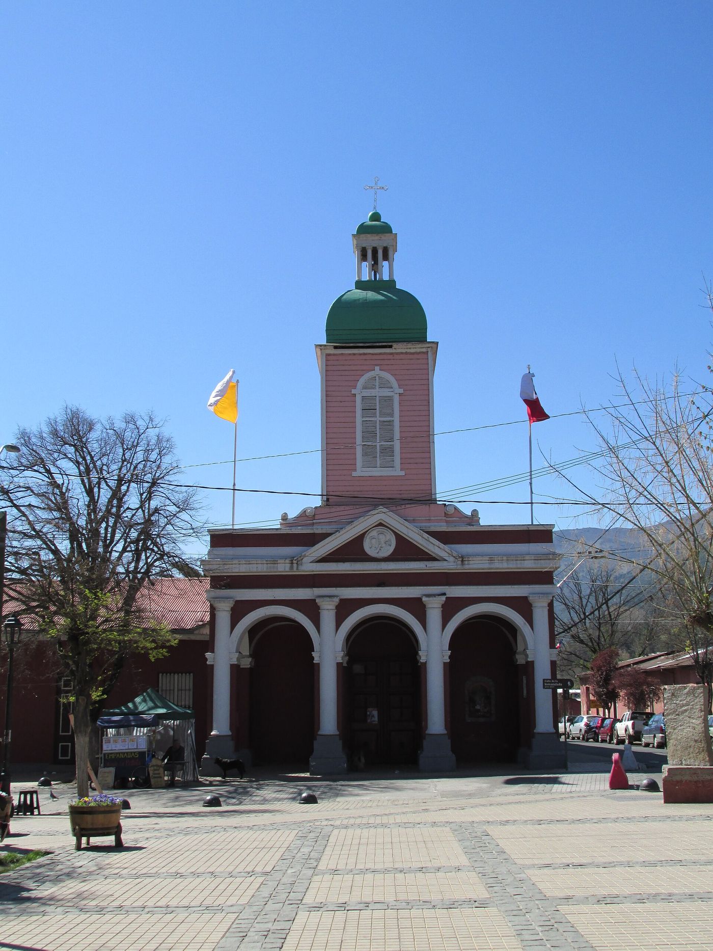 The pink and red church with a green-domed bell tower on the plaza of San José de Maipo