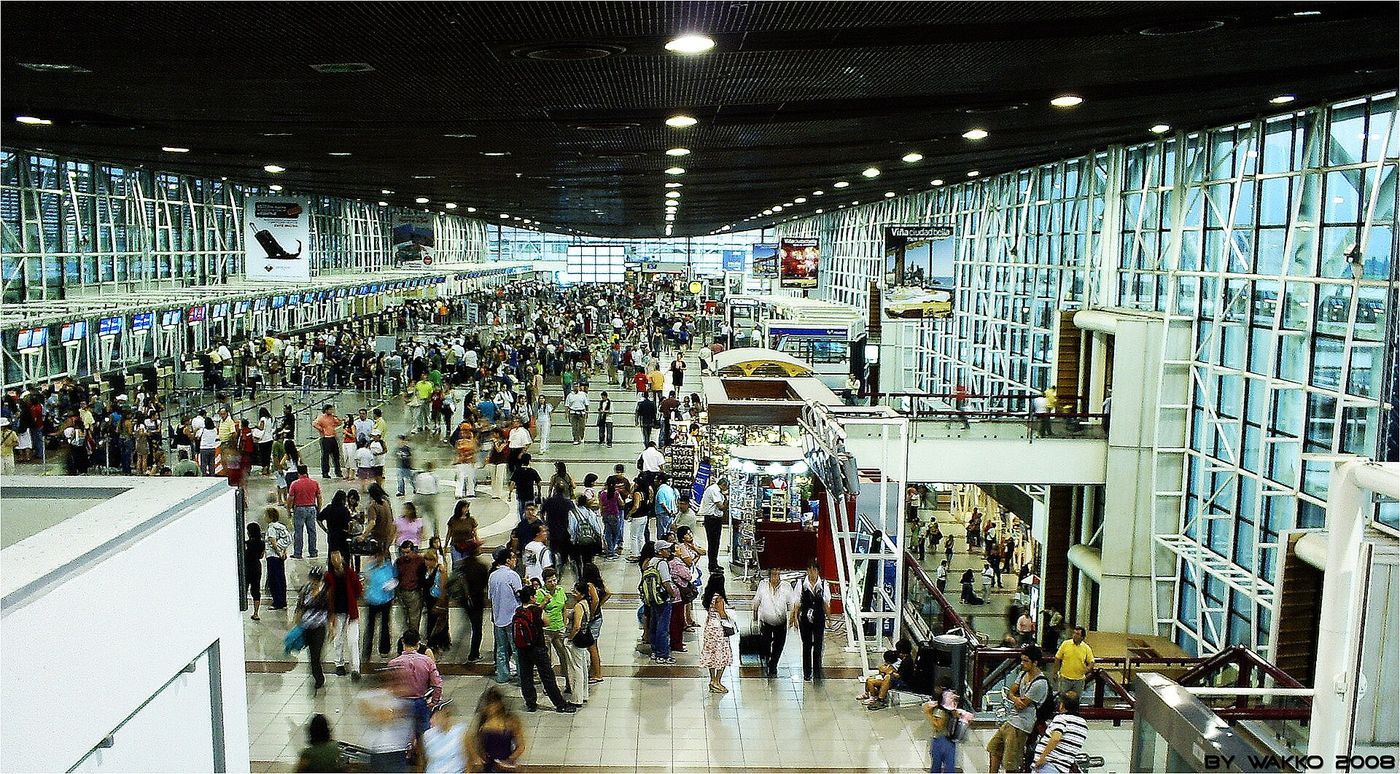 A busy check-in hall at Santiago airport with long glass walls and crowds of passengers