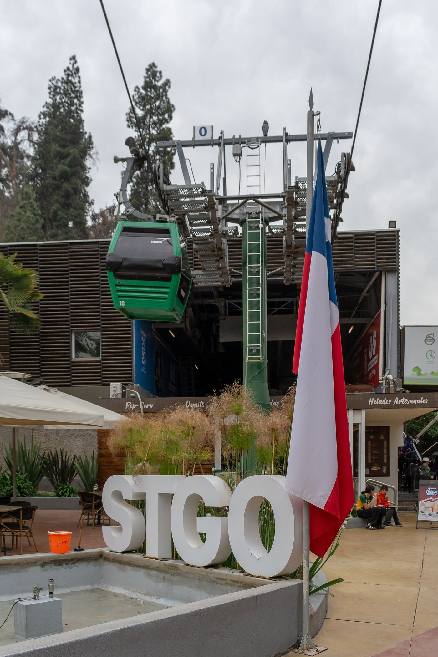 A green cable car at the Oasis station of the Santiago teleférico, with STGO letters and a Chilean flag in front