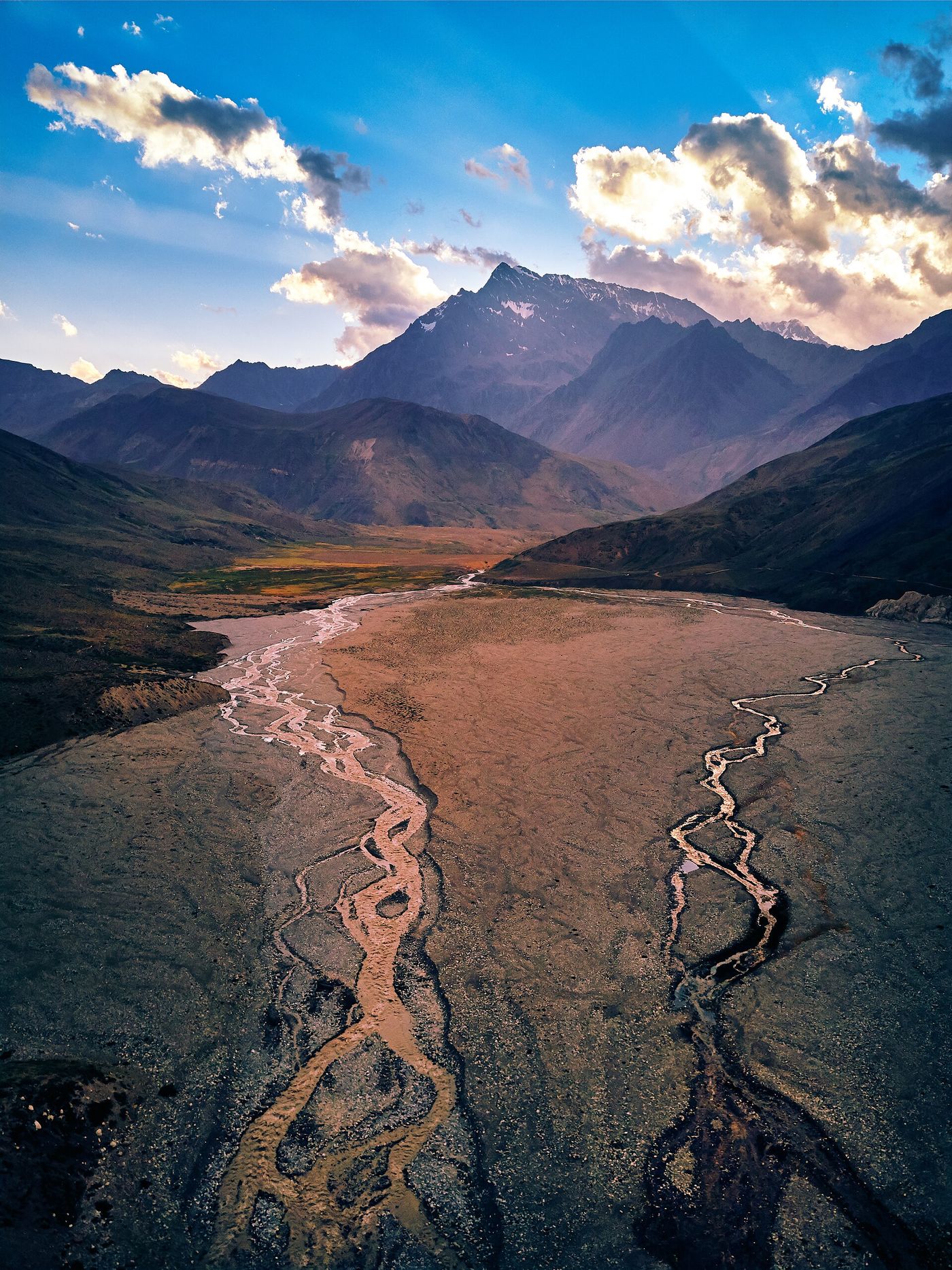 A braided river crossing a wide reddish valley floor toward high peaks near the Termas del Plomo