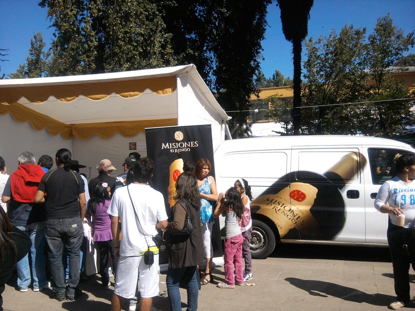 Visitors queuing at a winery tent beside a van painted with a giant wine bottle at a Chilean harvest festival