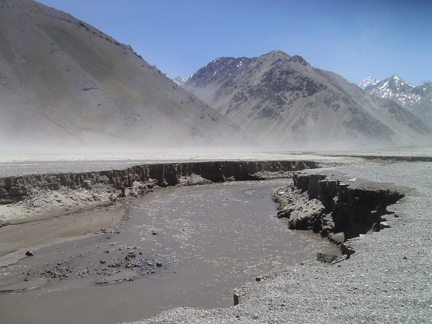 Wind lifting dust across a dry riverbed in the Yeso valley below bare mountains