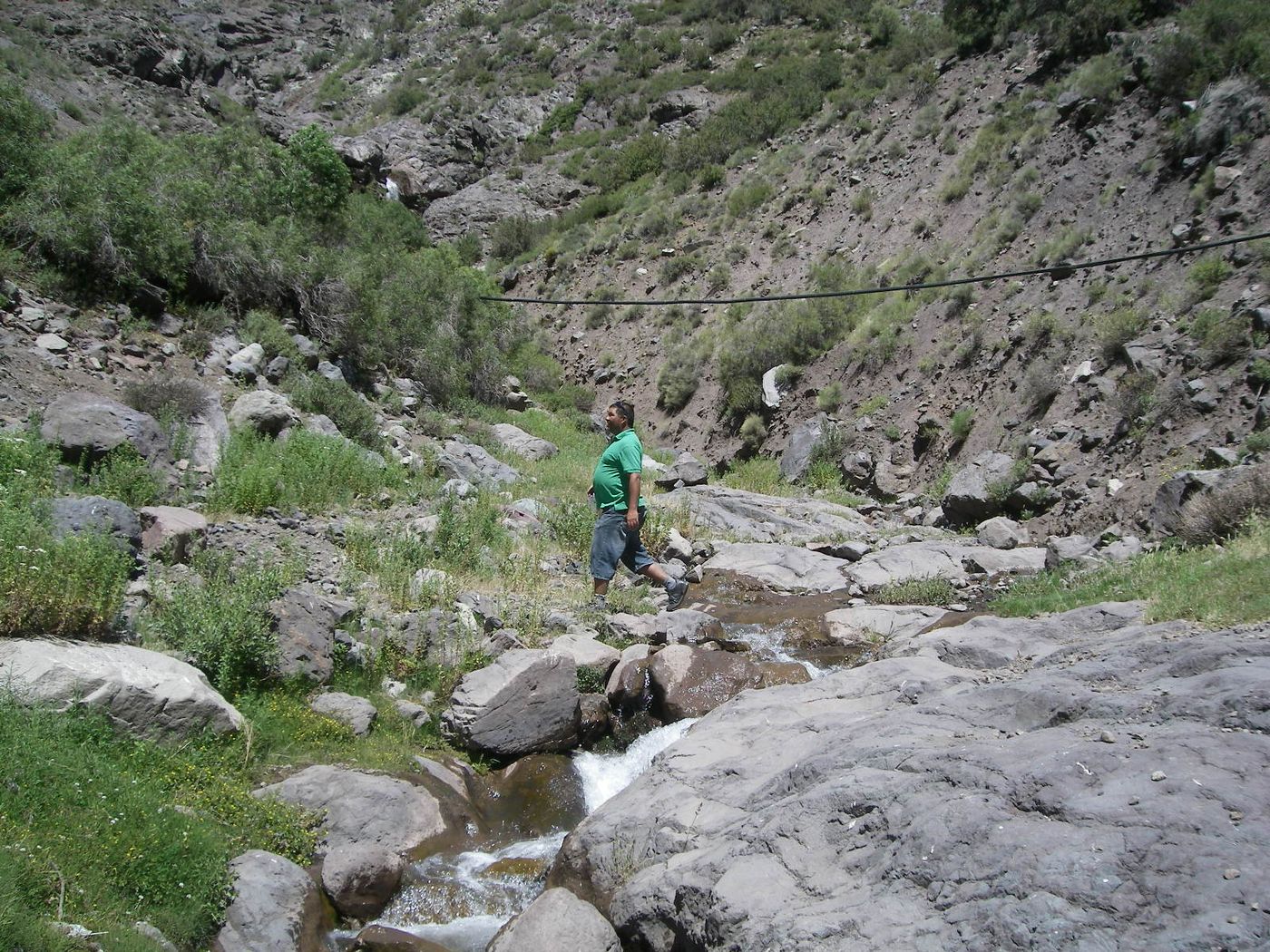 A hiker beside a rocky mountain stream in the Yeso valley, among boulders and green scrub